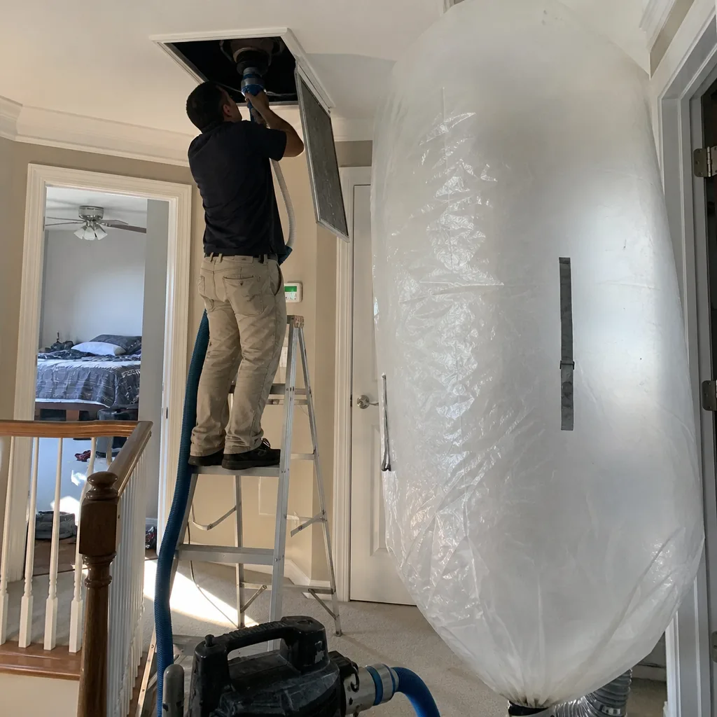 Technician performing professional residential air duct cleaning service with vacuum equipment